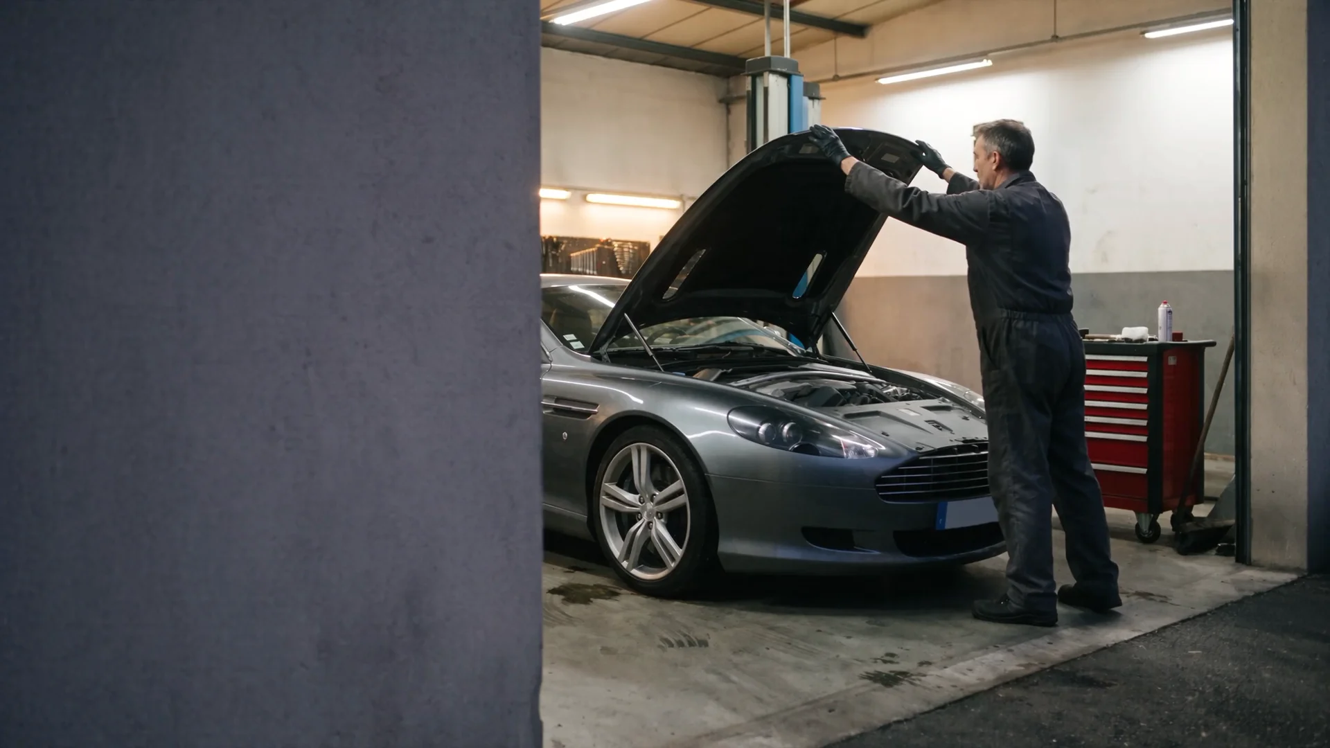 Un mécanicien et un coupé gris dans le garage fictif Atelier 07.